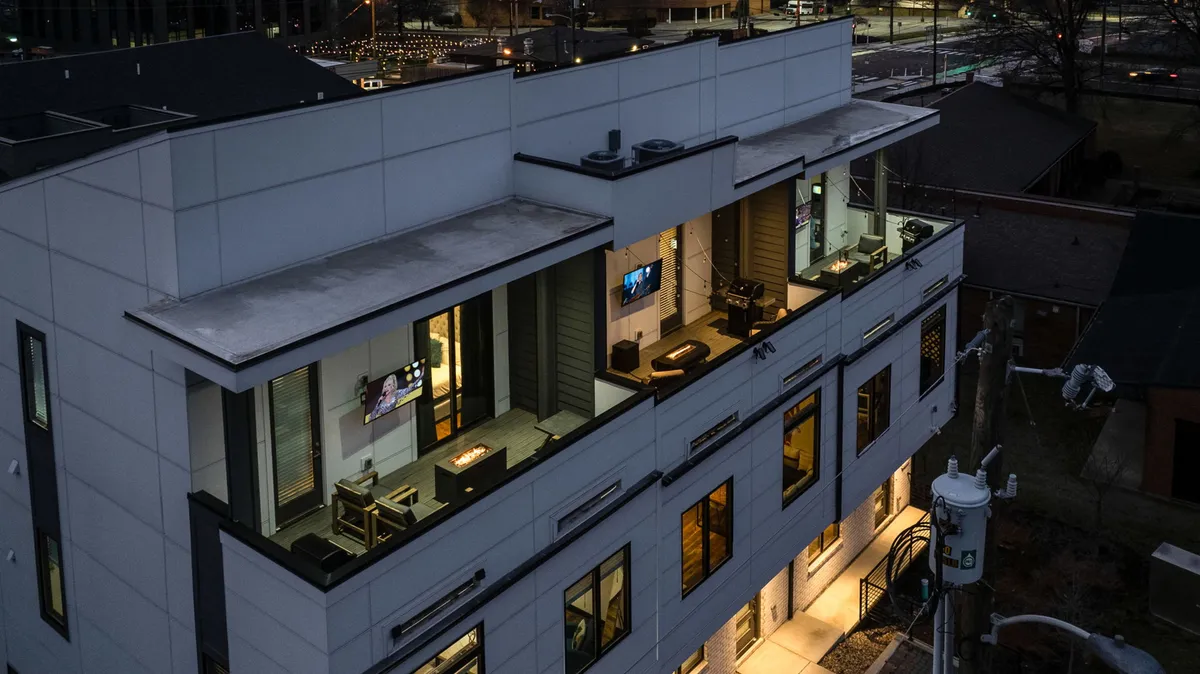 A contemporary exterior with balconies featuring outdoor furniture, large windows, and softly illuminated spaces, suggesting an inviting atmosphere for evening entertaining. The scene evokes the experience of relaxing outdoors or hosting friends while enjoying city lights.