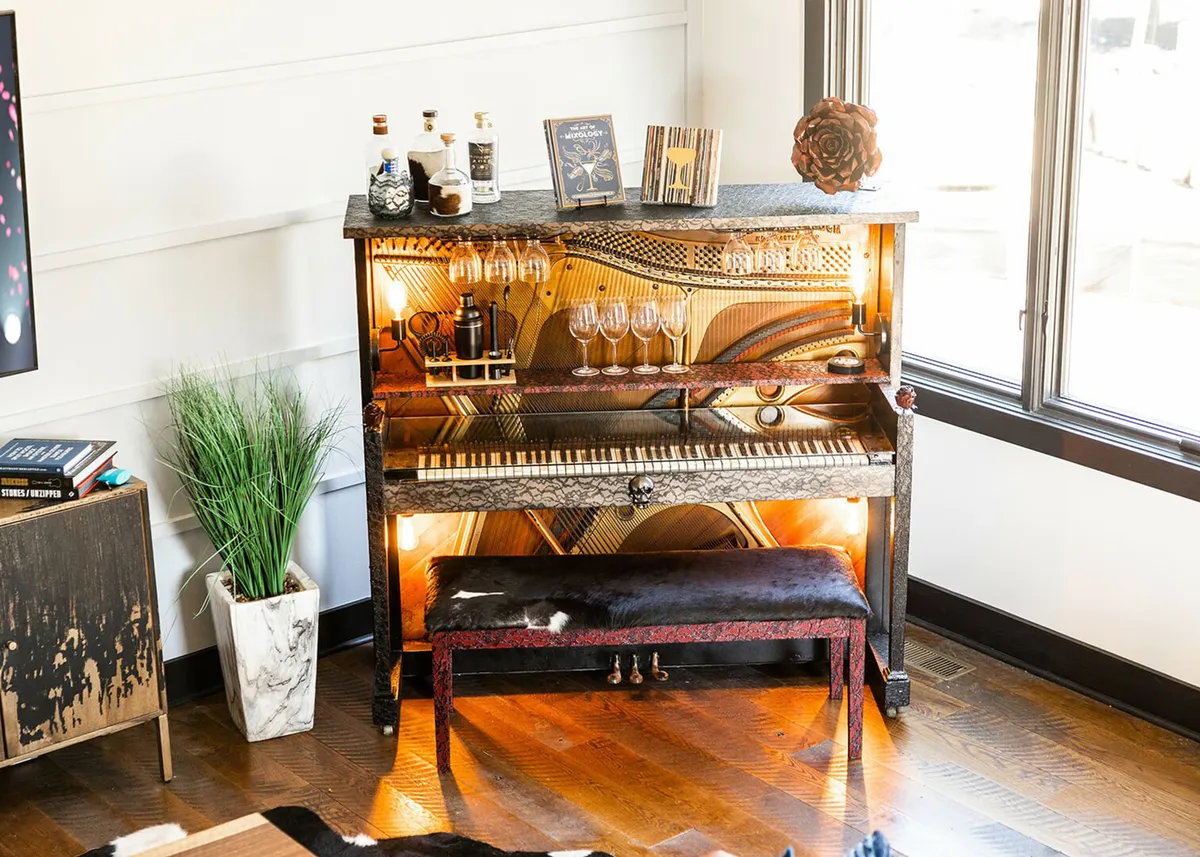 An inviting interior shot featuring a repurposed piano bar, decorative glassware, bottles of liquor, and touches of personal décor. The setup suggests an intimate space for music, socializing, and creative cocktails.