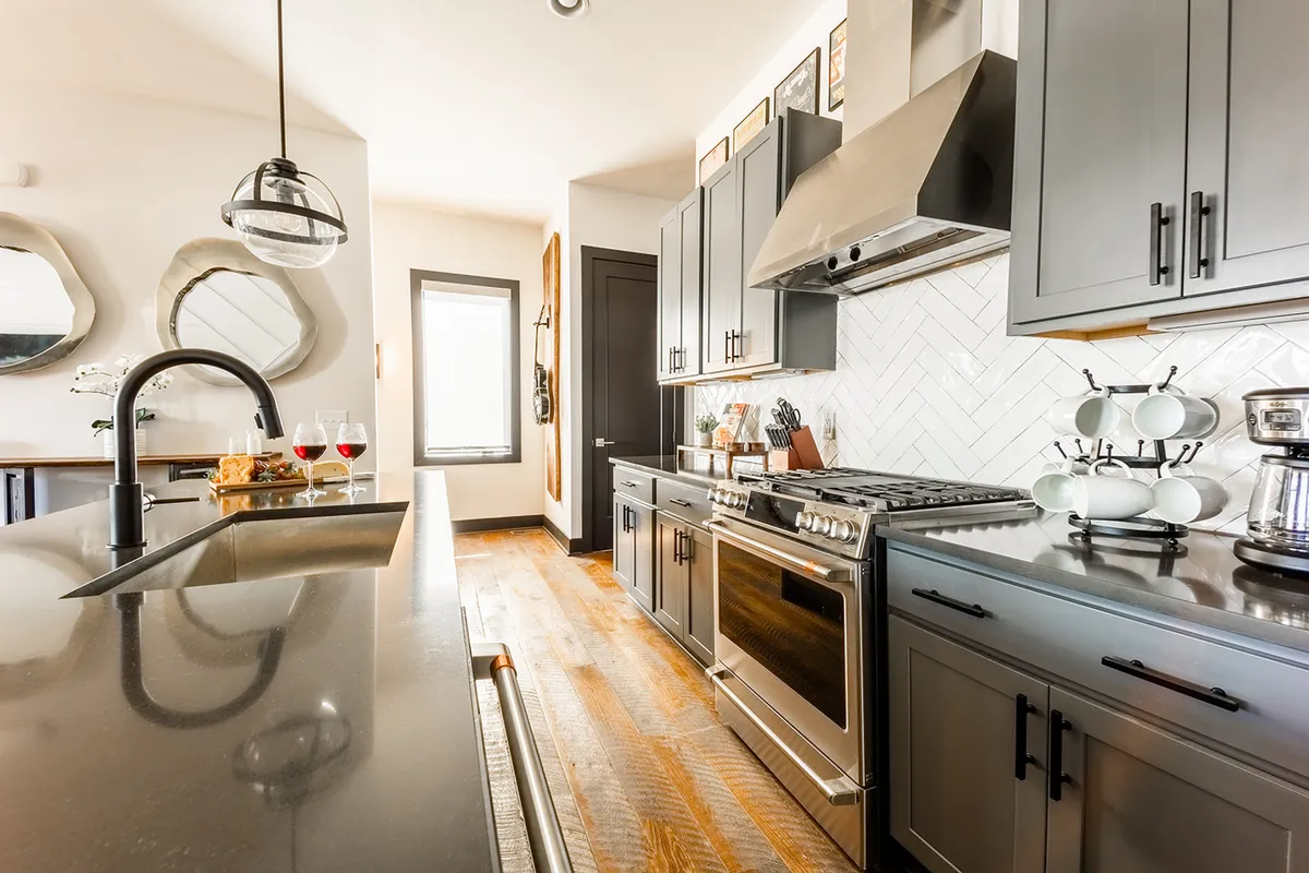 A contemporary kitchen scene with a large island countertop, stainless steel appliances gleaming under natural light, unique mirrors, and a bright window. The ambiance is cozy yet modern, with ample room for cooking and casual brunches with friends or family.
