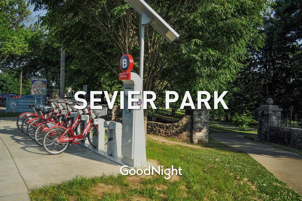An inviting park entrance featuring a bike rental station, solar panel, and green space. The scene is energetic, with pathways for walking and biking, suggesting active family outings and connection to nature.